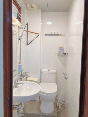 Une petite salle de bain avec un lavabo, des toilettes et une douche, le tout de couleur blanche.
