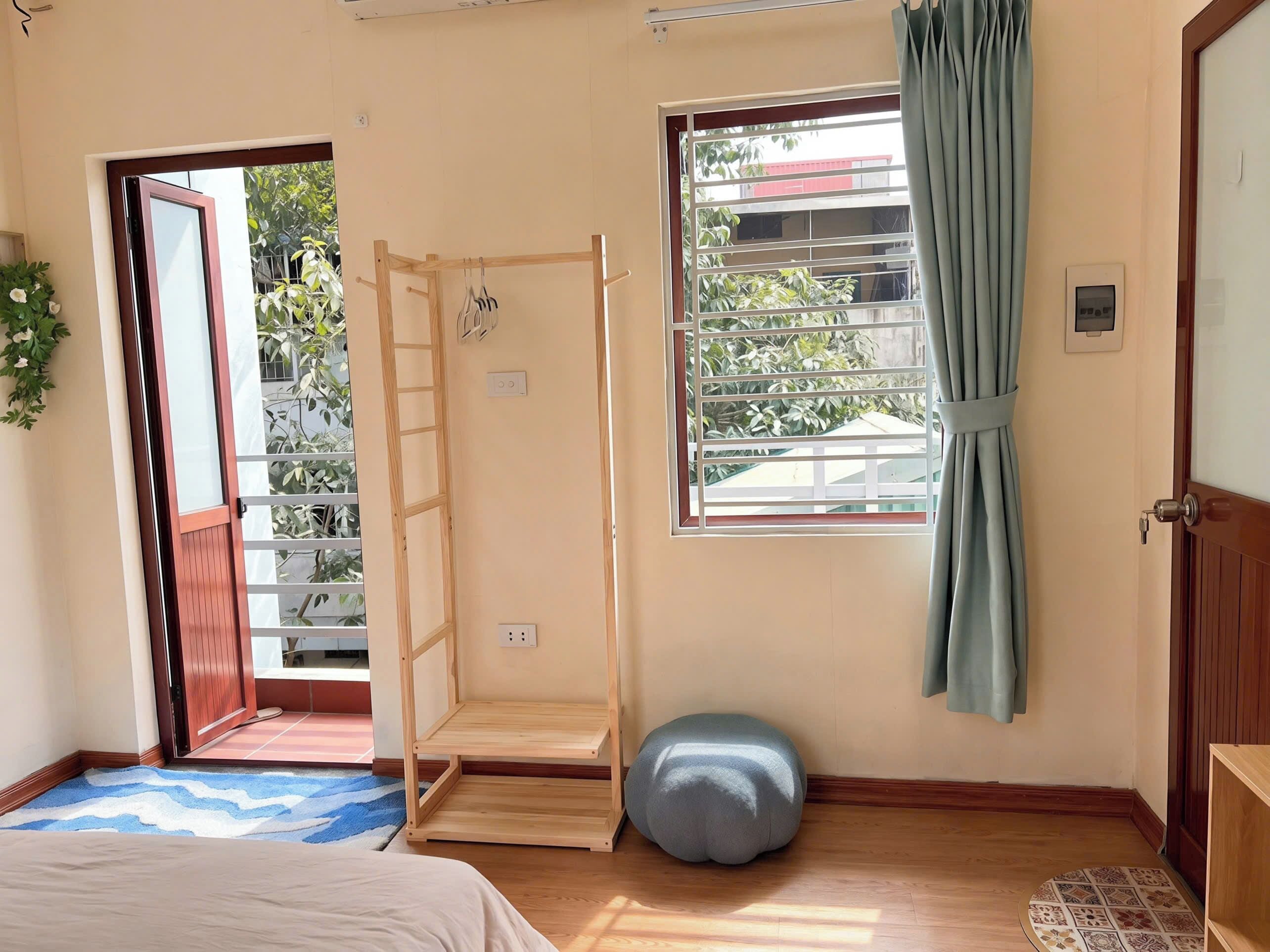 Una habitación con cama, una escalera de madera, una ventana con cortinas y un taburete pequeño.