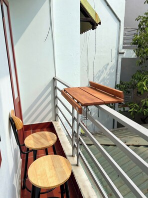 Un balcon avec deux tables en bois et un banc, une balustrade blanche et une petite fenêtre.