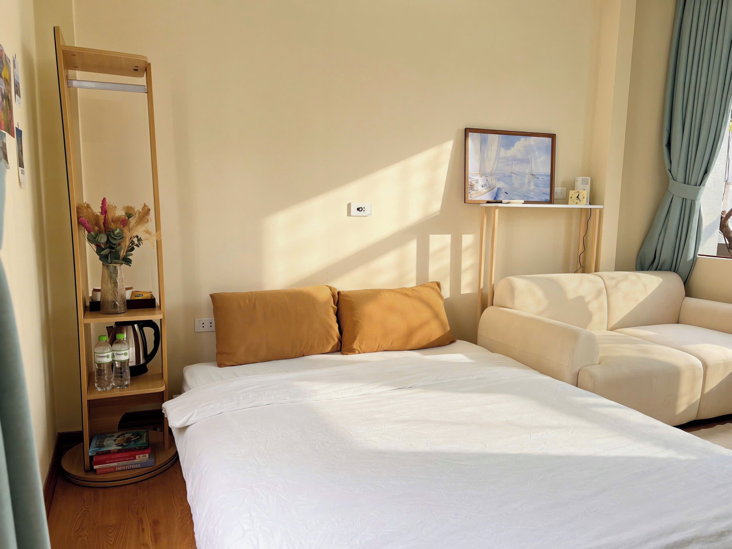 Ein Hotelzimmer mit einem Bett, einer Couch, einem Spiegel, einem Regal mit Büchern und einer Vase sowie einem Gemälde an der Wand.