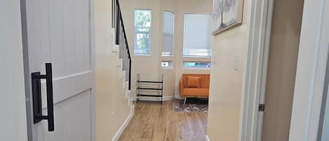 A hallway with a wooden floor, a sliding door, a staircase, and a sofa in the background.