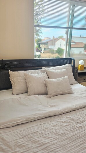 Una cama con cabecera, almohadas y vistas a casas a través de una ventana.