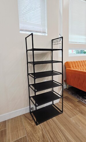 Une étagère métallique noire, composée de cinq étagères, placée contre un mur avec des fenêtres.