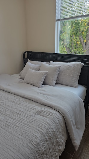 A bed with a headboard, a window with blinds, and a view of greenery outside. - Brand-New Modern 3BR/3BA Private ADU • A/C • High Ceilings • Canoga Park (Los Angeles)