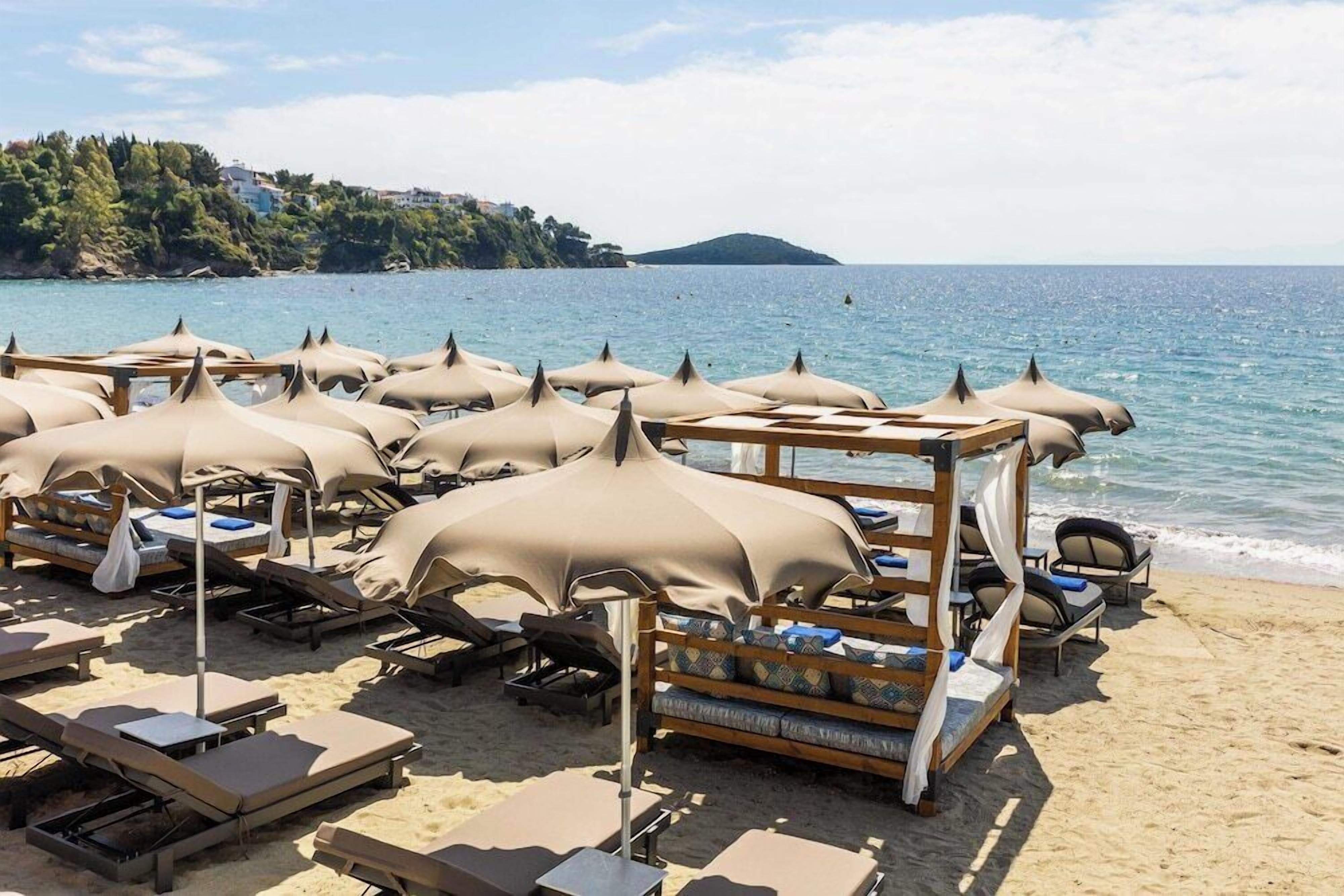 A beach with sunbeds and umbrellas, a wooden deck, and a view of the sea and a distant island.