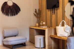 A modern room with a grey sofa, a wooden desk, a small stool, a wall-mounted TV, and a decorative wall hanging.