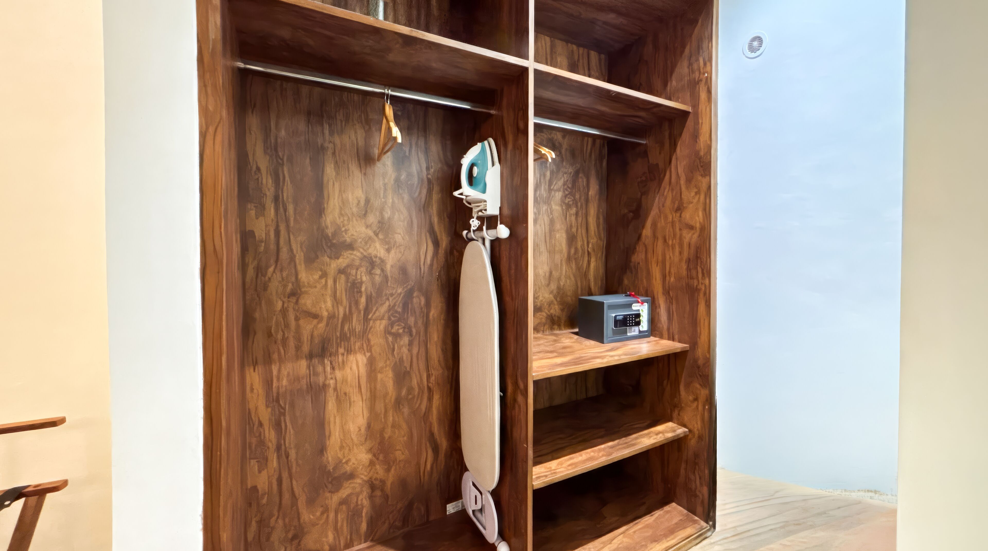 Un armario de madera con un plancha colgada y un estante pequeño con una caja fuerte.