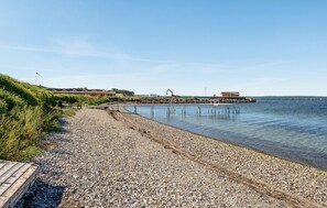 Ein Kiesstrand mit einer Holzstege, der zu einem Steg über ruhiges Wasser führt.