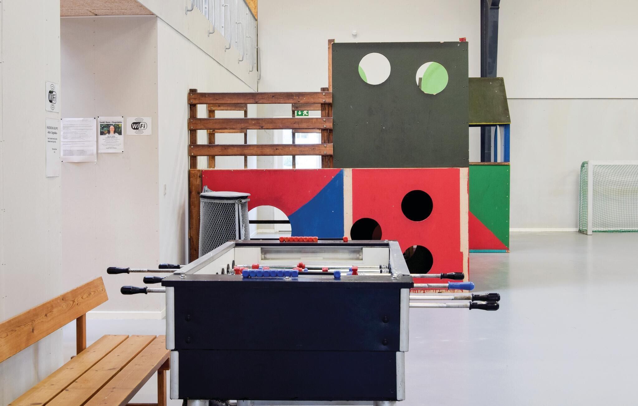A room with a foosball table, a wooden bench, and a wall with various papers and signs.