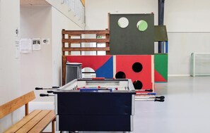 Ein Zimmer mit einem Kicker, einer Holzbank und einer Wand mit verschiedenen Papieren und Schildern.
