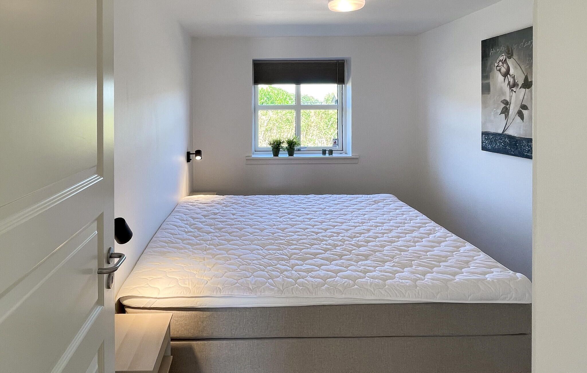 Une chambre à coucher avec un lit, une fenêtre ornée de plantes et un tableau accroché au mur.
