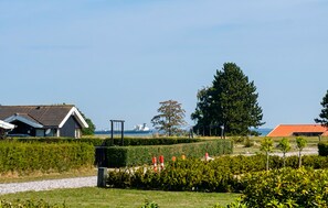 Ein Wohngebiet mit Häusern, einem großen Baum und einem Gewässer im Hintergrund.