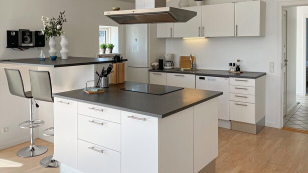 A modern kitchen with white cabinetry, a central island, and bar stools. - Gorgeous home in Rudkøbing with sauna (Rudkøbing)