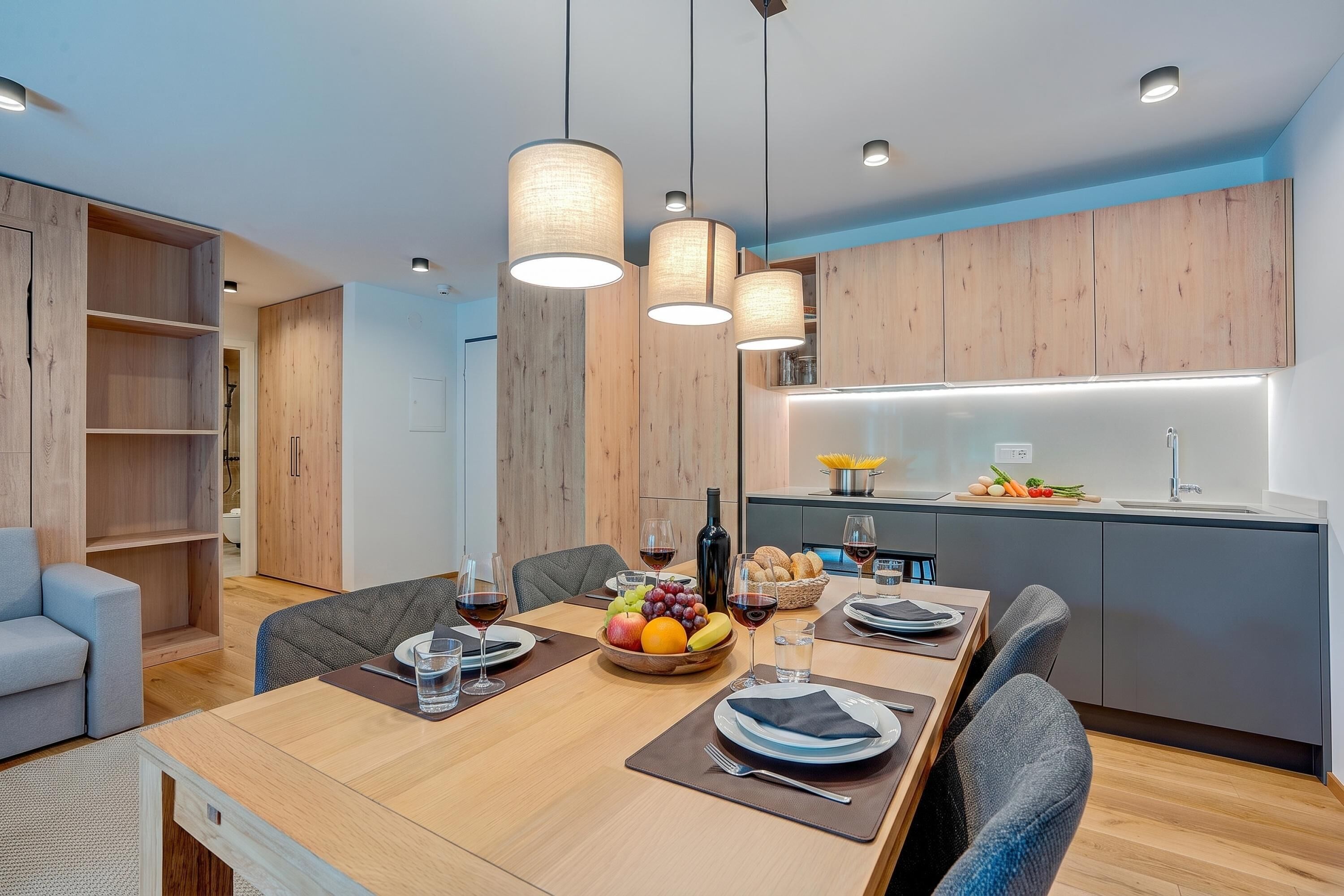 A modern dining area with a wooden table set for four, a kitchen with a built-in island, and a seating area with a sofa and chairs.