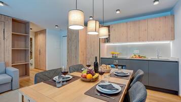 A modern dining area with a wooden table set for four, a kitchen with a built-in island, and a seating area with a sofa and chairs.