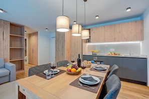 A modern dining area with a wooden table set for four, a kitchen with a built-in island, and a seating area with a sofa and chairs. - Residenza Castanea (Mesocco)