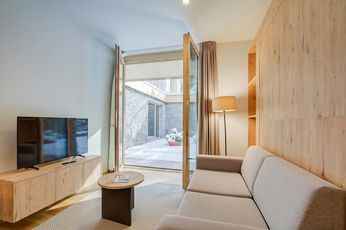 A modern living room with a flat-screen TV, a sofa, a coffee table, and a view of a snowy outdoor area through a glass door.