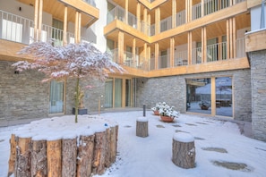 A multi-level wooden building with balconies, stone walls, and snow-covered outdoor seating areas. - Residenza Castanea (Mesocco)