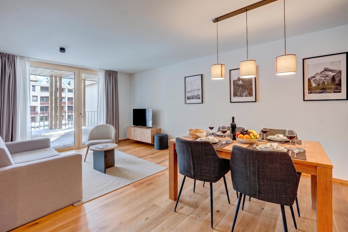 A modern living room with a sofa, a dining table set for two, and a TV.