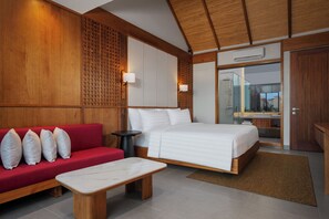 A hotel room with a bed, a red sofa, a small table, and a bathroom visible through an open door. - Seahaven Villas By Kamuela (Canggu)