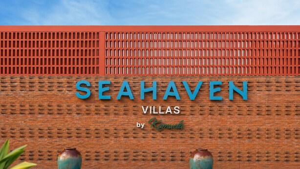 Un muro de ladrillo con el texto 'SEAHAVEN VILLAS by Kamula' y dos grandes jarrones.