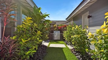 A residential backyard with a lawn, a grill, and various plants.