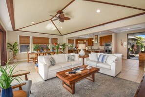 Ein geräumiger Wohnbereich mit Deckenventilator, zwei weißen Sofas, einem Holztisch und einem Essbereich mit Tisch und Stühlen.