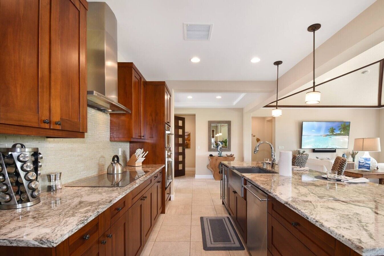 A modern kitchen with wooden cabinets, granite countertops, stainless steel appliances, and a dining area with a TV and seating.