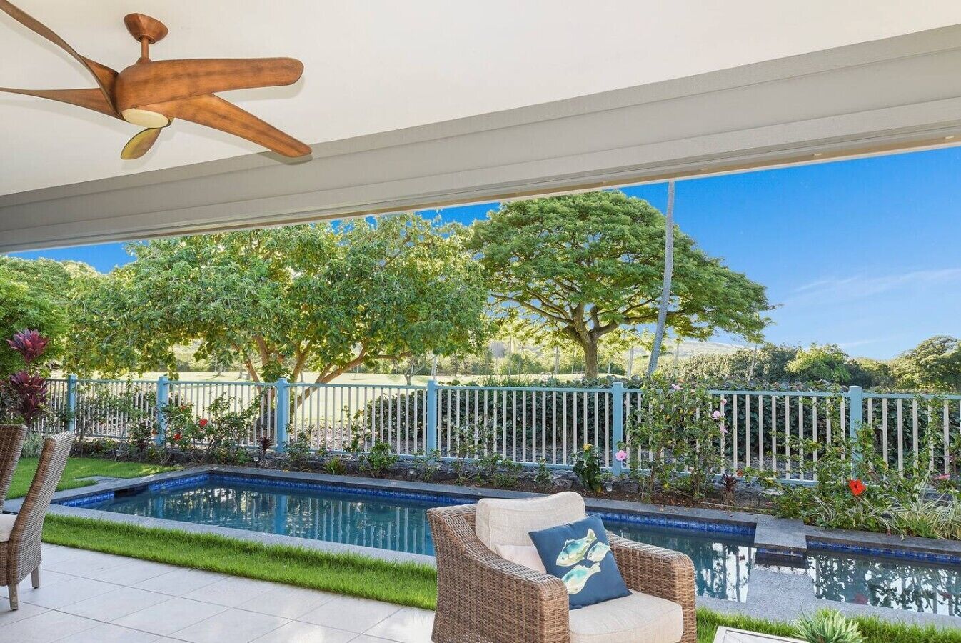 A covered outdoor area with a pool, wicker furniture, and a ceiling fan.