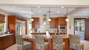 A modern kitchen with wooden cabinets, stainless steel appliances, and a central island with woven chairs.