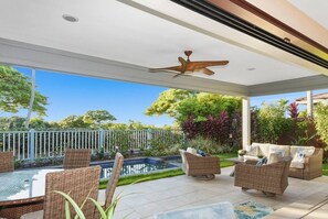 A covered outdoor area with wicker furniture, a ceiling fan, and a view of a pool and garden. - Island Time-Luxury Golf Front Home with Pool/Spa (Kailua-Kona)