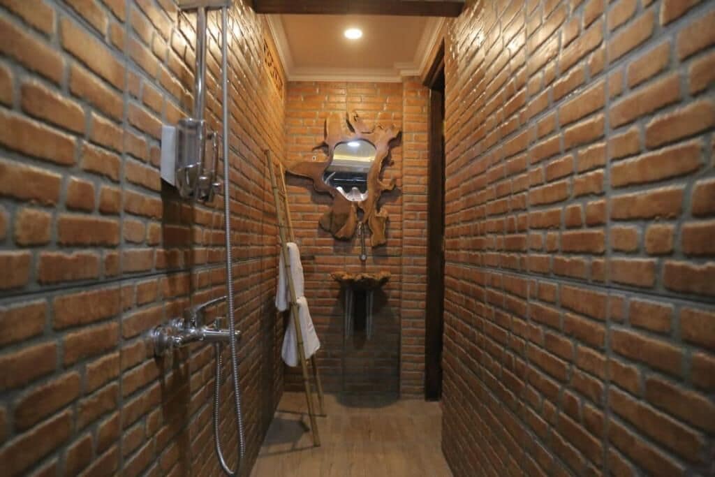 A narrow hallway with brick walls, a wooden floor, and a shower area with a towel rack.