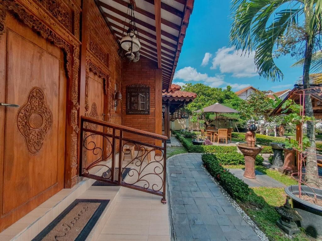 A wooden building with intricate carvings, a metal railing, and a pathway leading to a garden area with outdoor furniture.