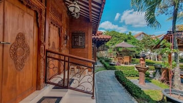 A wooden building with intricate carvings, a metal railing, and a pathway leading to a garden area with outdoor furniture.
