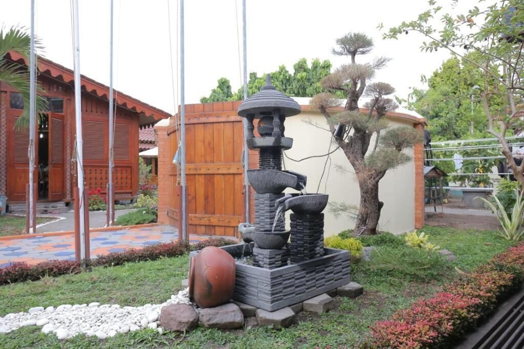 Un jardín con una fuente de piedra, una valla de madera y un edificio con tejado de baldosas.