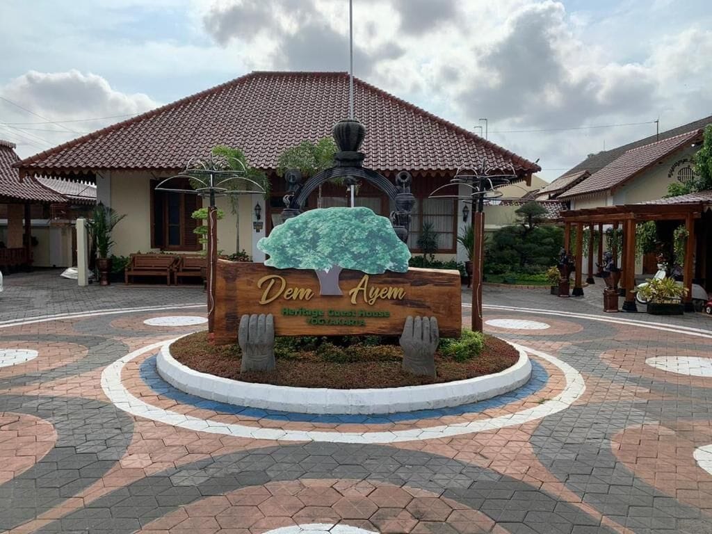 Una plaza circular con un letrero de madera en el centro que dice 'Dem Ayem', rodeada de un pavimento con un diseño decorativo.