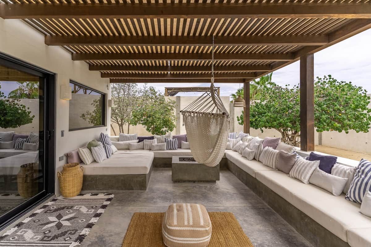 Un área de estar al aire libre con pérgola, sofás acolchados y una silla colgante.
