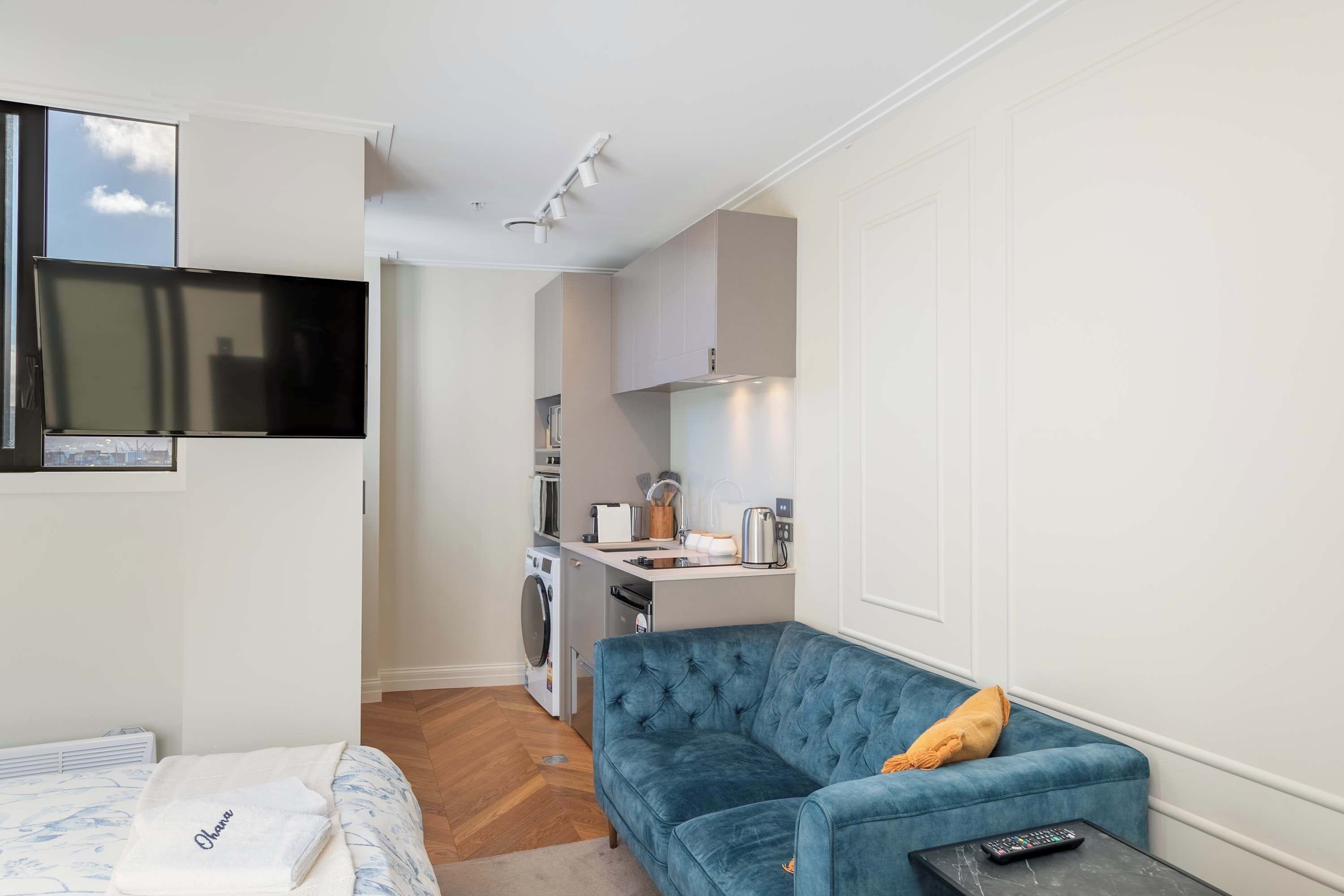 A compact living space with a sofa, a flat-screen TV, a kitchen area, and a washing machine.