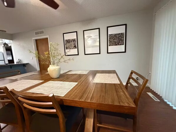 A dining area with a wooden table, chairs, and a vase with flowers. There are three framed pictures on the wall. - Luxury Casa Sequoia (Dinuba)