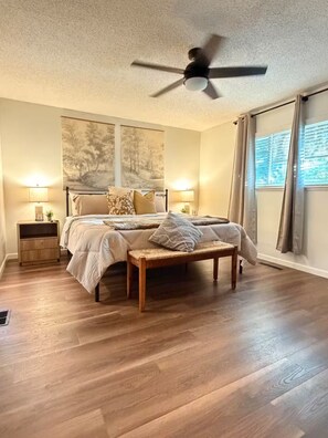 A bedroom with a bed, bedside tables, a ceiling fan, and a large window with curtains. - Luxury Casa Sequoia (Dinuba)