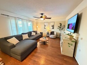 A living room with a sofa, armchairs, a coffee table, a TV, a ceiling fan, and a window with curtains. - Luxury Casa Sequoia (Dinuba)