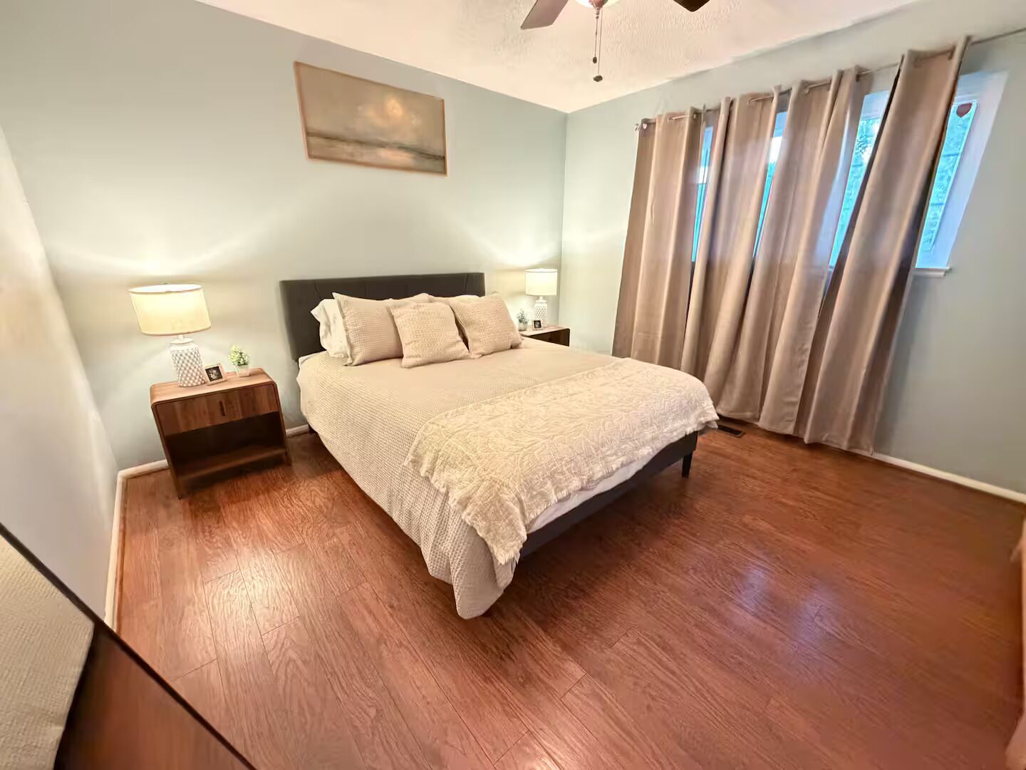 A bedroom with a bed, nightstands, a ceiling fan, and a window with curtains.