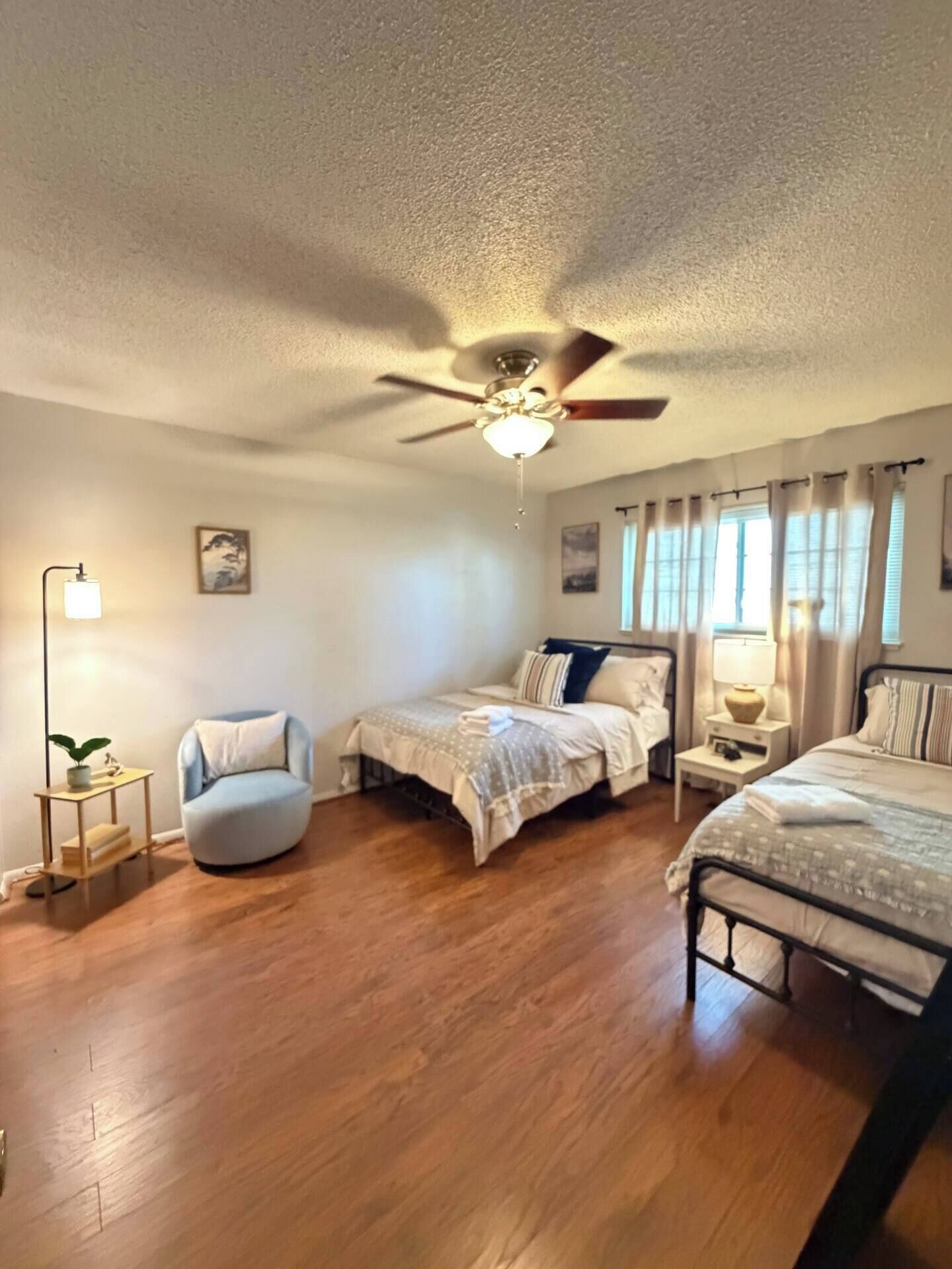 A bedroom with two beds, a ceiling fan, a floor lamp, and a small table with a plant.