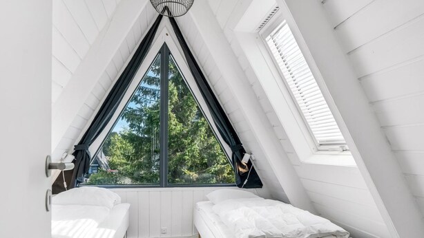 Una habitación con techo inclinado, dos camas, una ventana y una puerta.