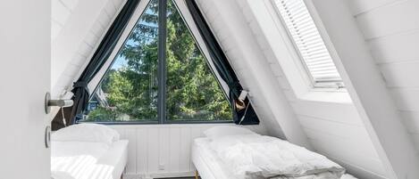 Ein Zimmer mit schrägen Wänden, zwei Betten, einem Fenster und einer Tür.