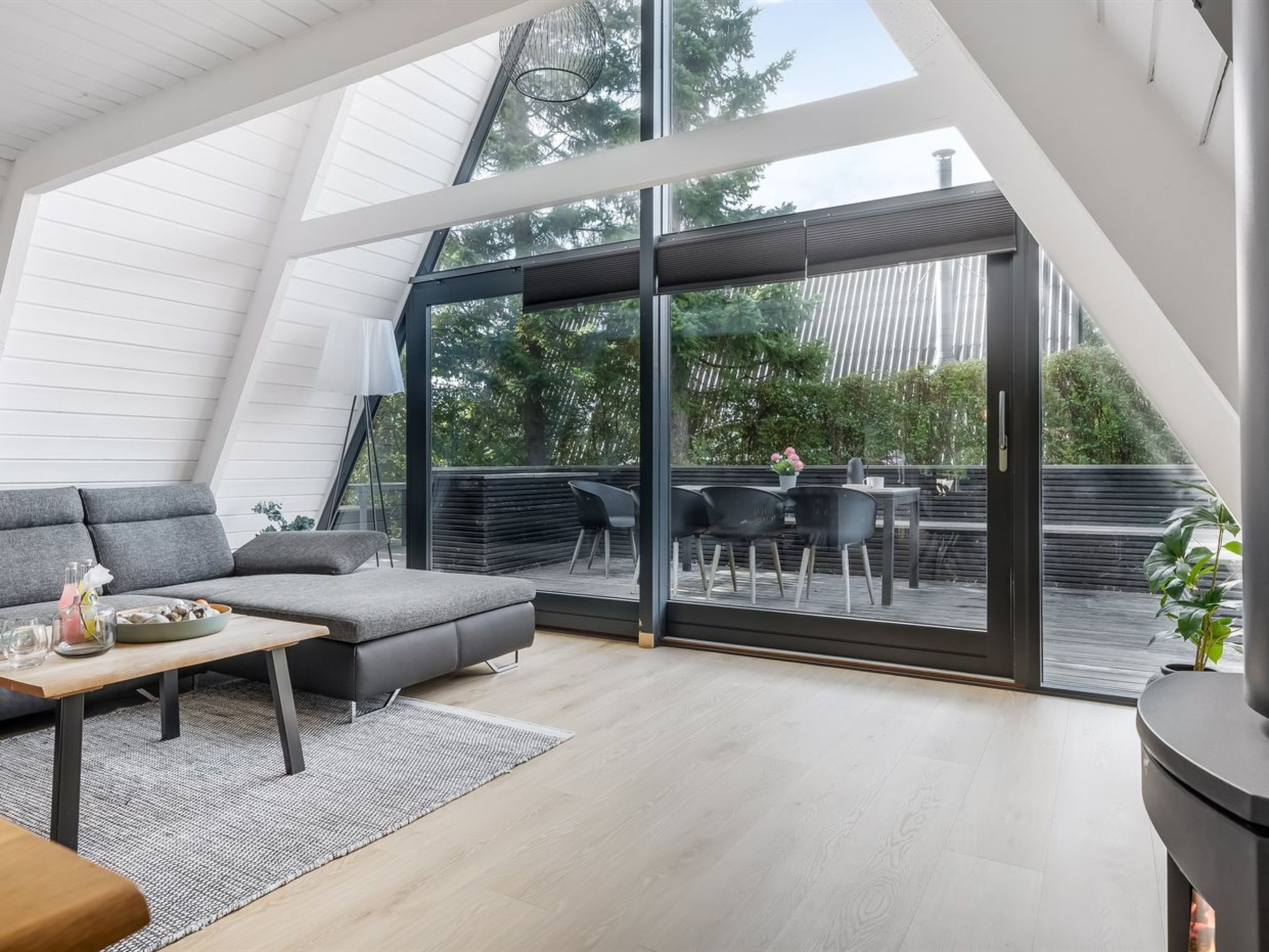 A modern interior with a sloped ceiling, a grey sofa, a small table, and a dining area with chairs.
