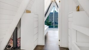 Un pasillo estrecho con paredes blancas y suelo de madera que conduce a un dormitorio con cama y ventana.