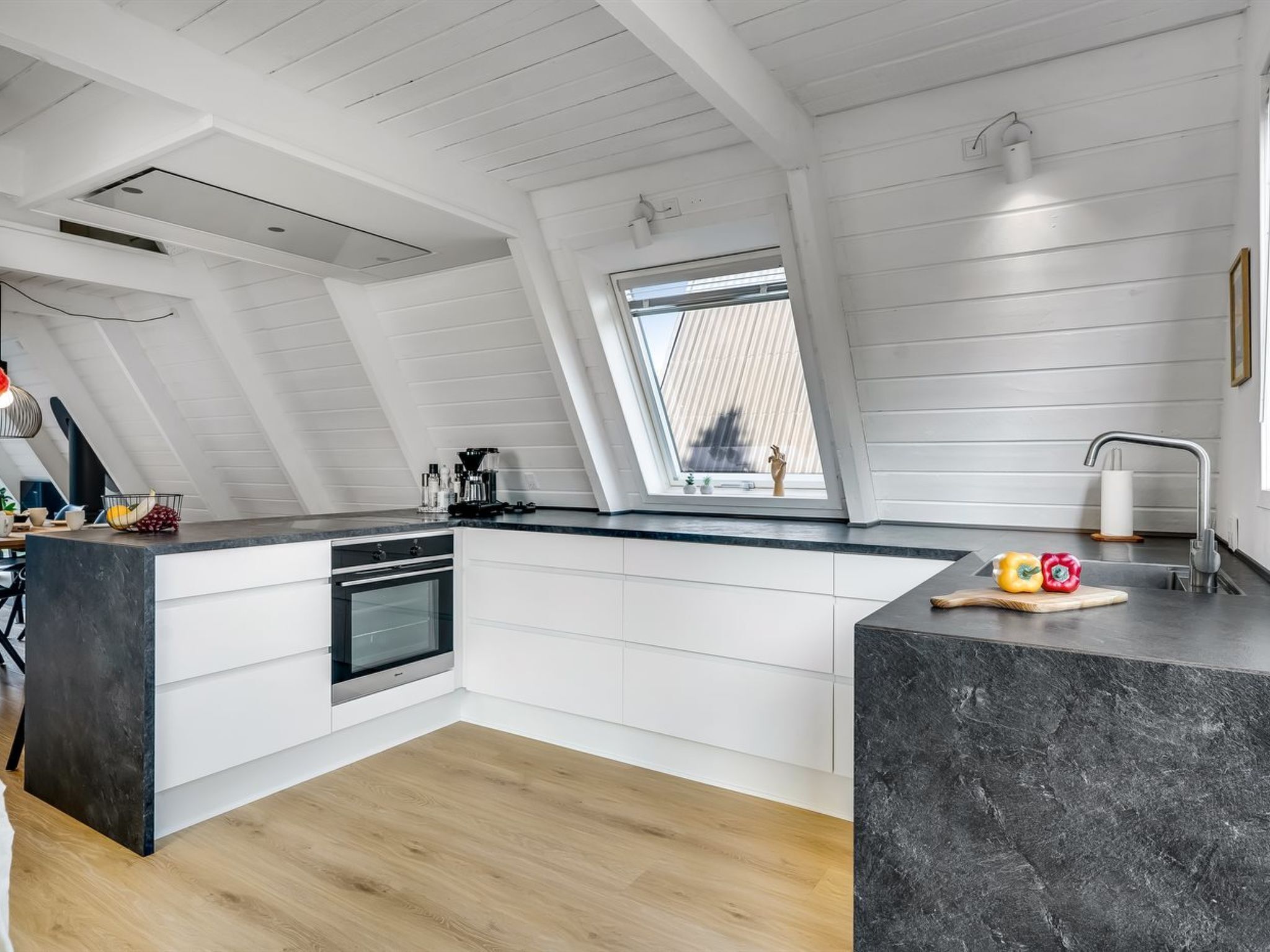 A modern kitchen with a skylight, white cabinetry, and a black marble countertop.