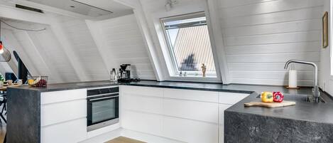 A modern kitchen with a skylight, white cabinetry, and a black marble countertop.