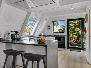 Ett modernt kök med en central köksö, barstolar, en diskmaskin och ett stort fönster.